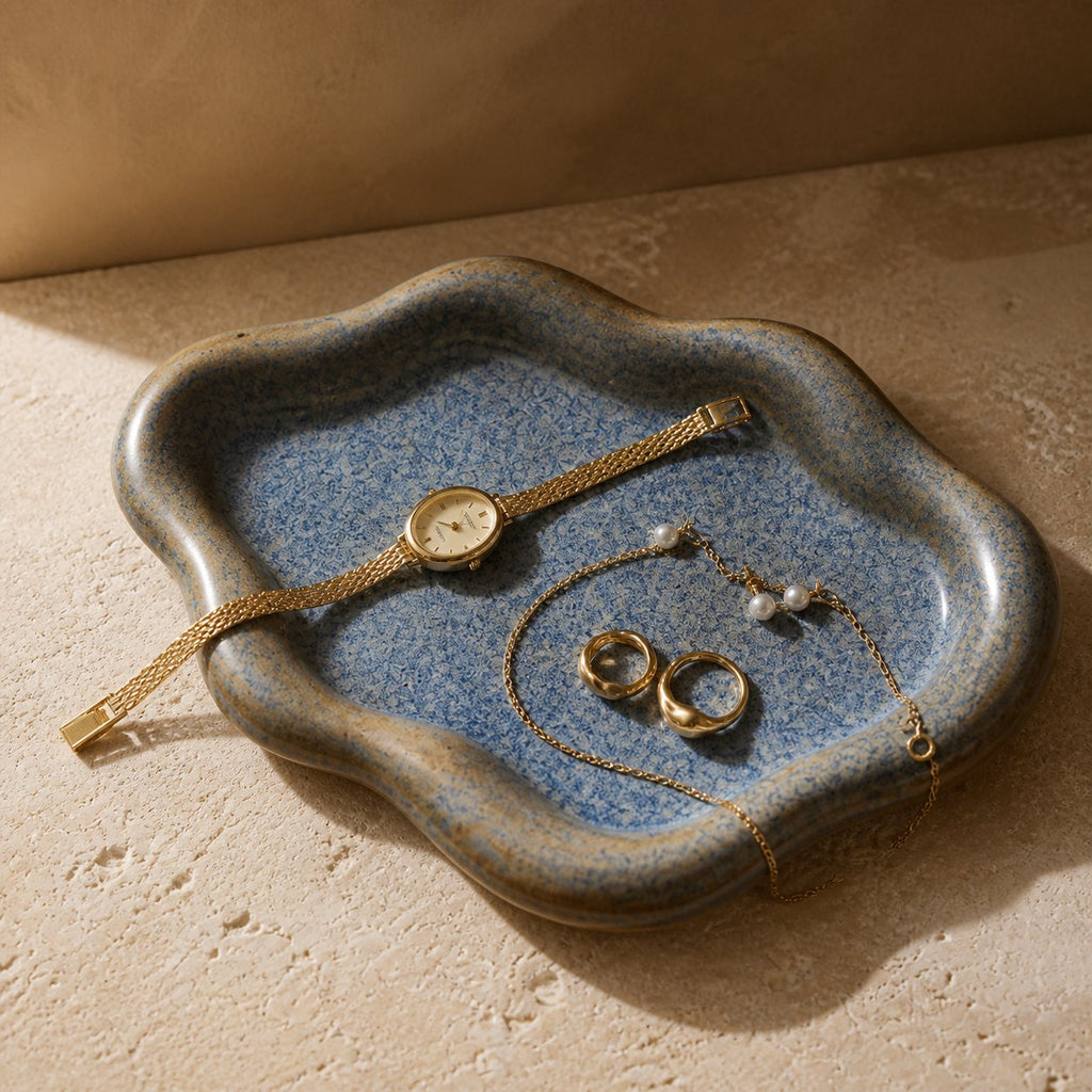 Blue-gray cloud-shaped ceramic jewelry tray holding a gold-tone watch, bracelet, rings and pearl earrings.