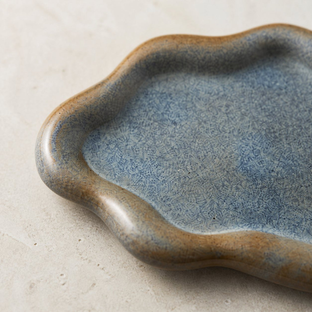 Close-up of blue-gray speckled ceramic glaze and warm brown rim on a cloud-shaped catchall tray.