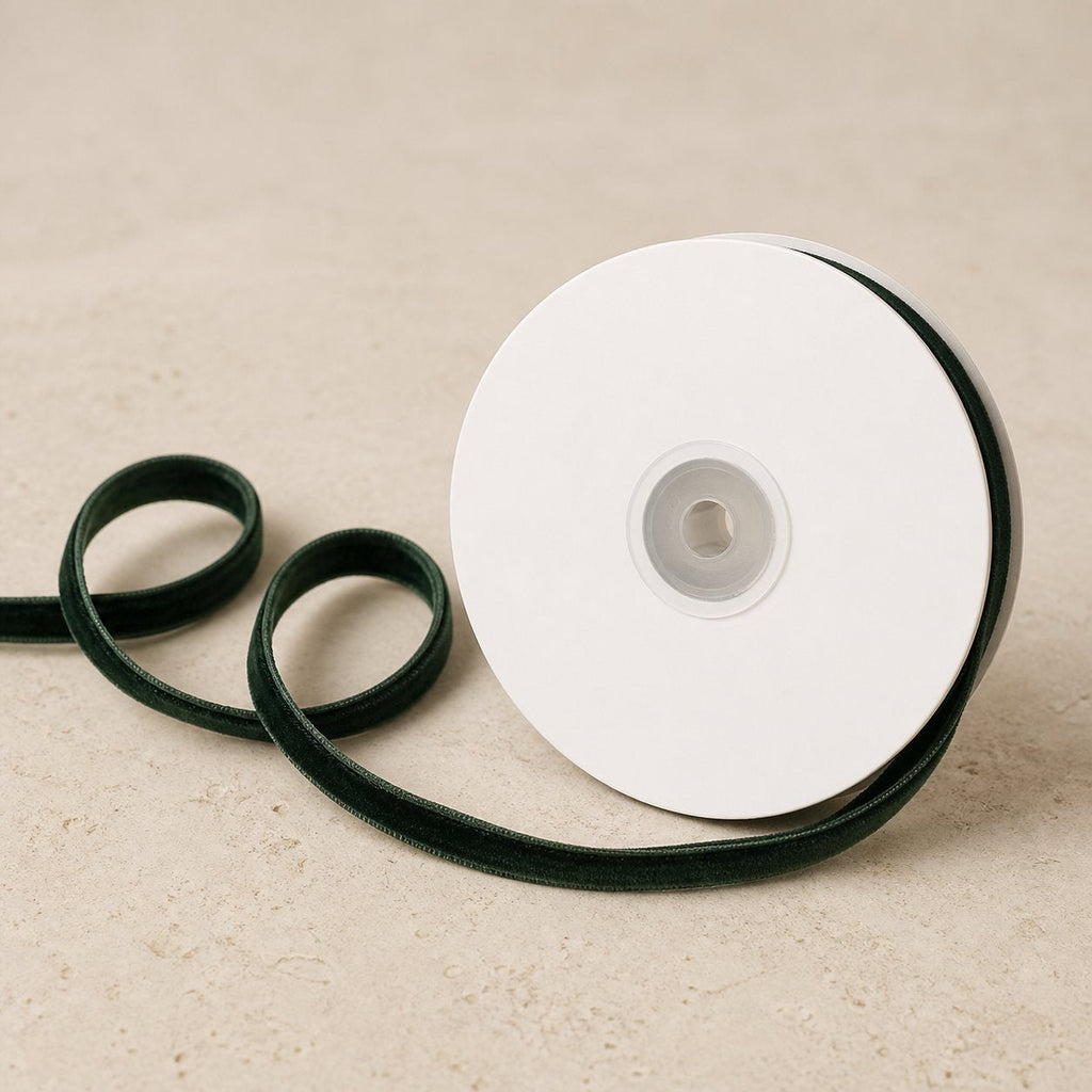 Deep Jade Green double-sided velvet ribbon unwinding from a plain white spool on warm limestone.
