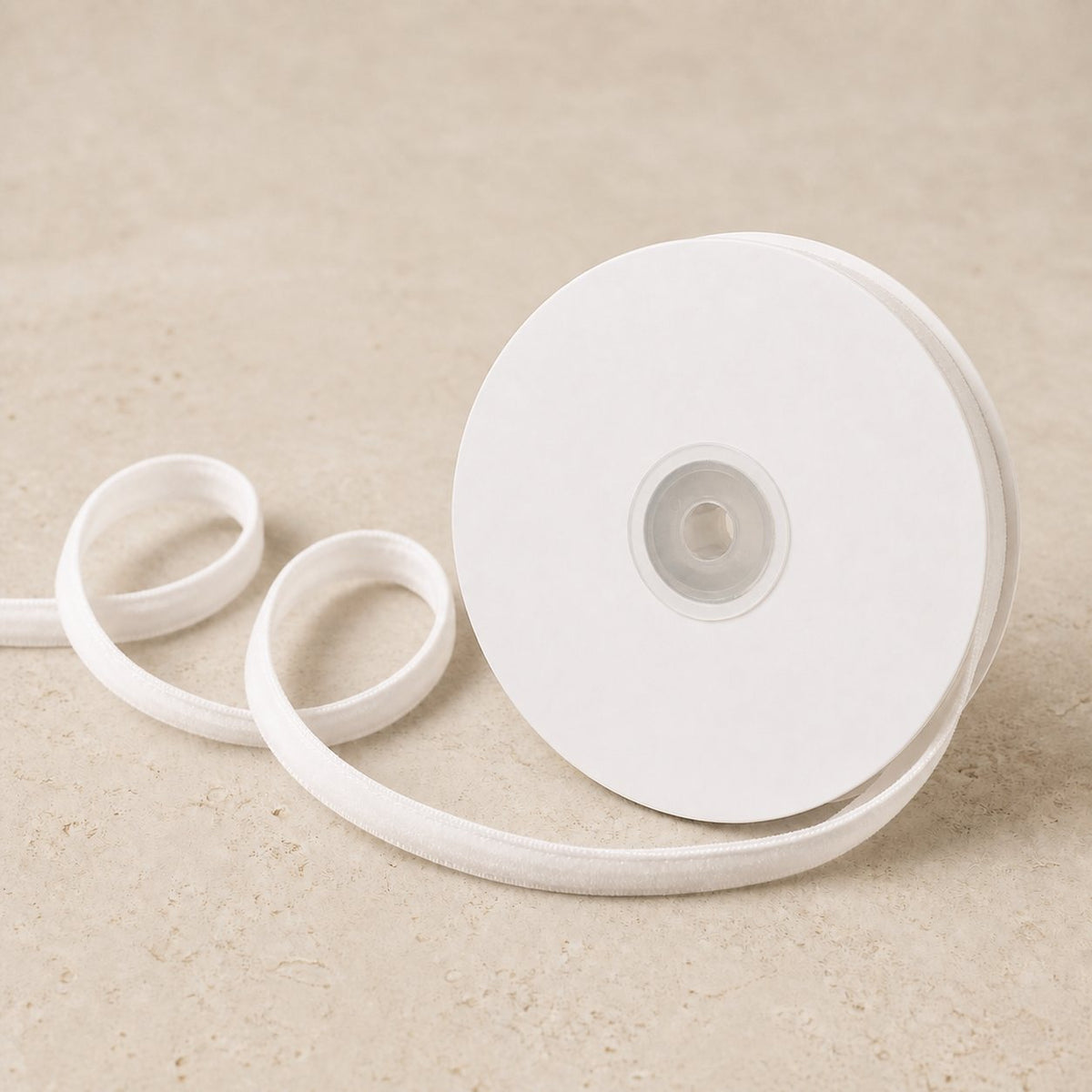 Ivory White double-sided velvet ribbon unwinding continuously from a plain white spool on warm limestone.