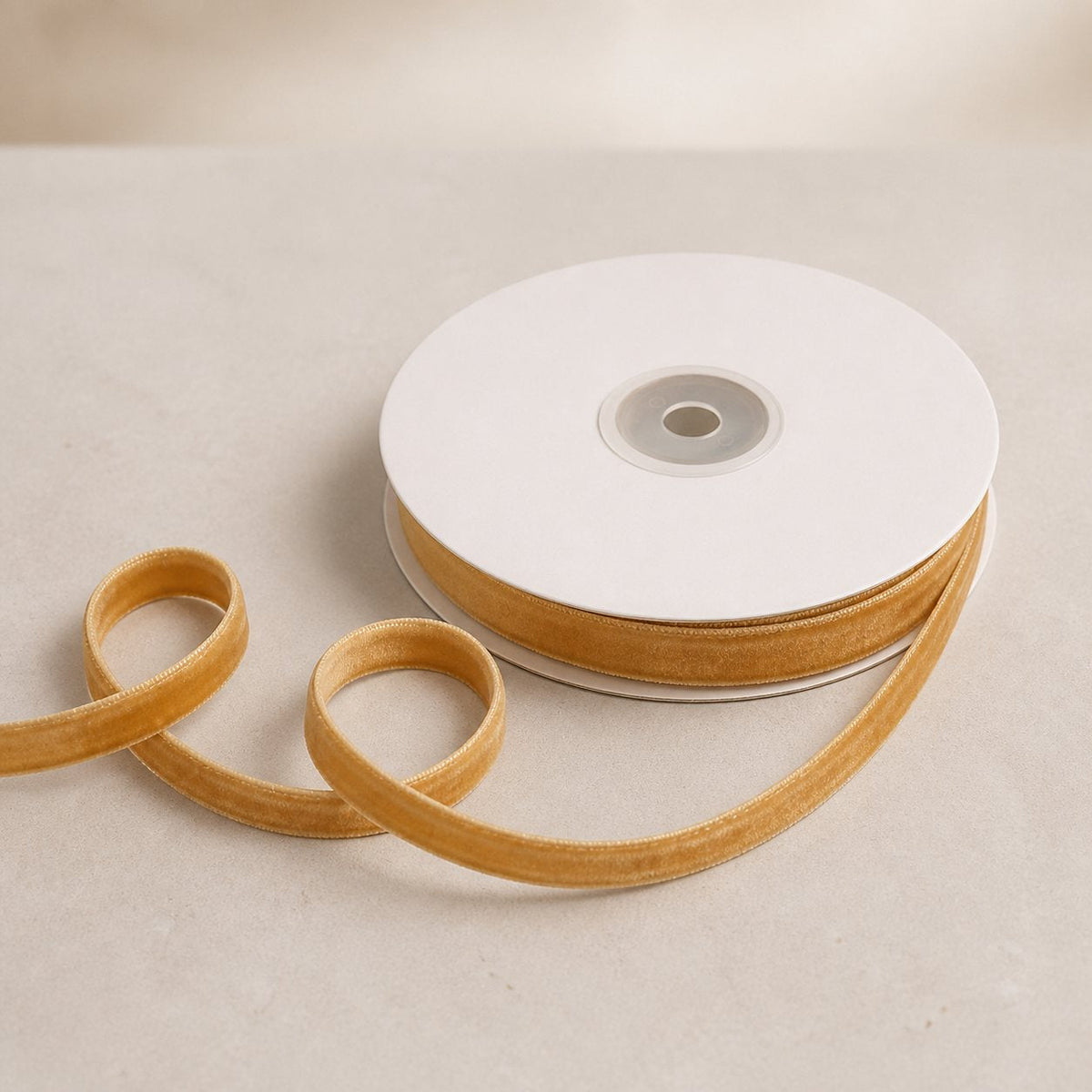 Antique Gold double-sided velvet ribbon on a plain white spool with a loose ribbon curve on warm limestone.