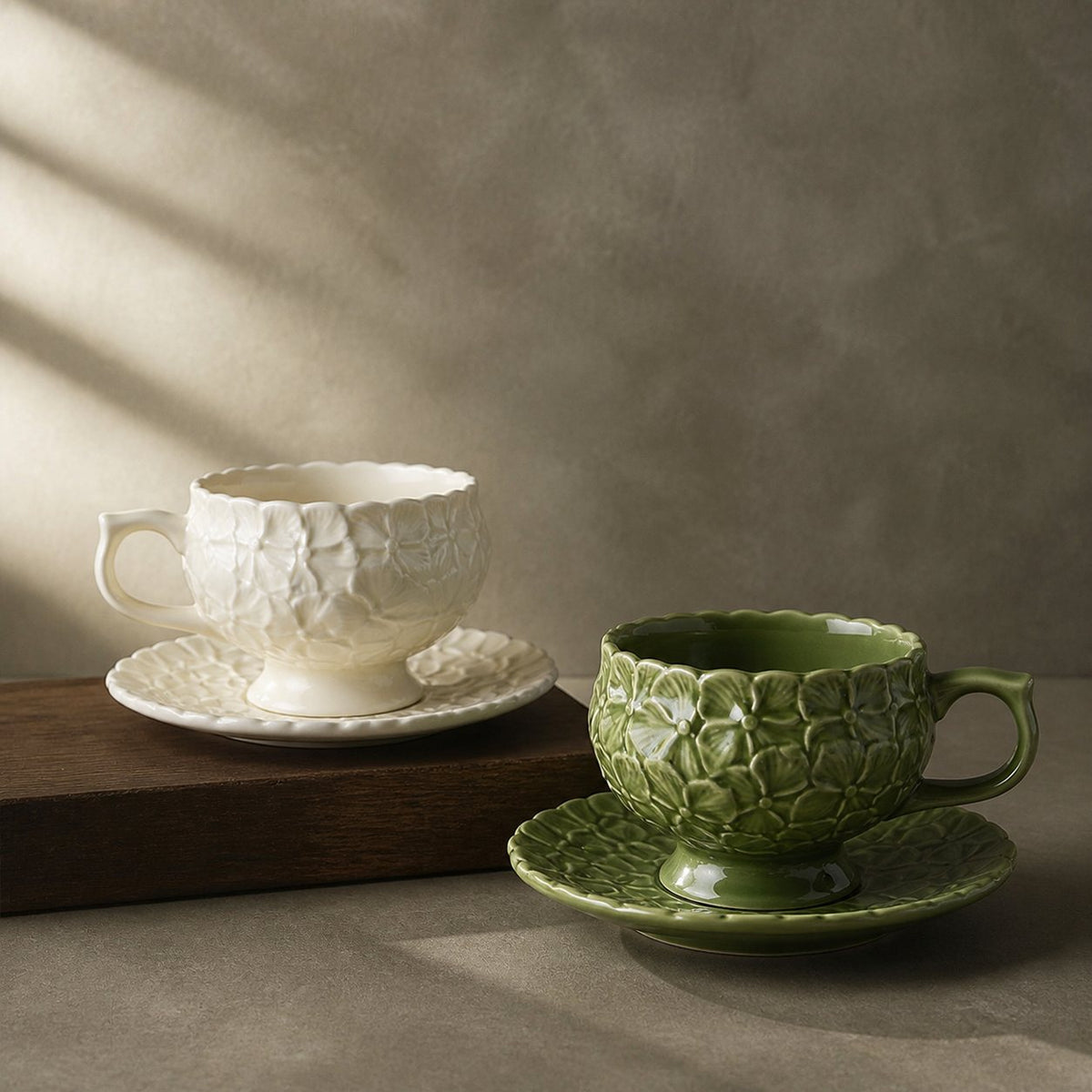 Ivory Bloom and Sage Garden hydrangea relief ceramic cups with matching saucers on warm wood and stone.