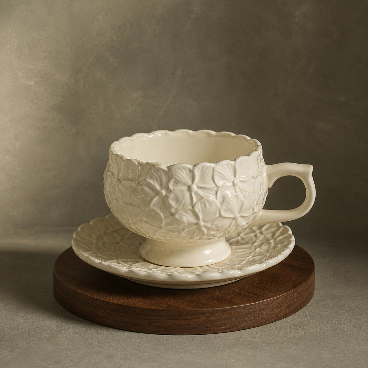 Ivory Bloom ceramic cup and saucer with raised hydrangea petals on a round walnut stand.