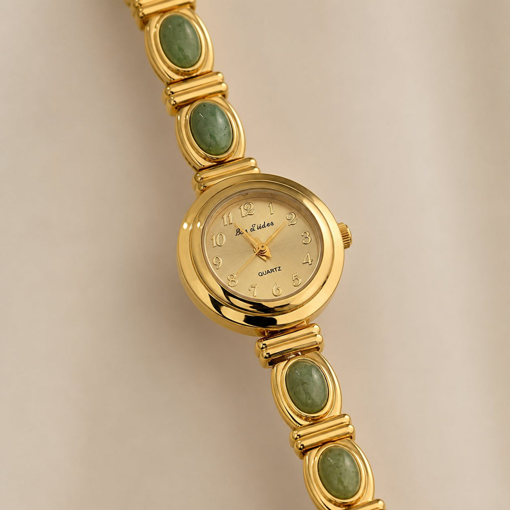 Close-up of a gold-tone alloy watch dial framed by four oval green inlays.