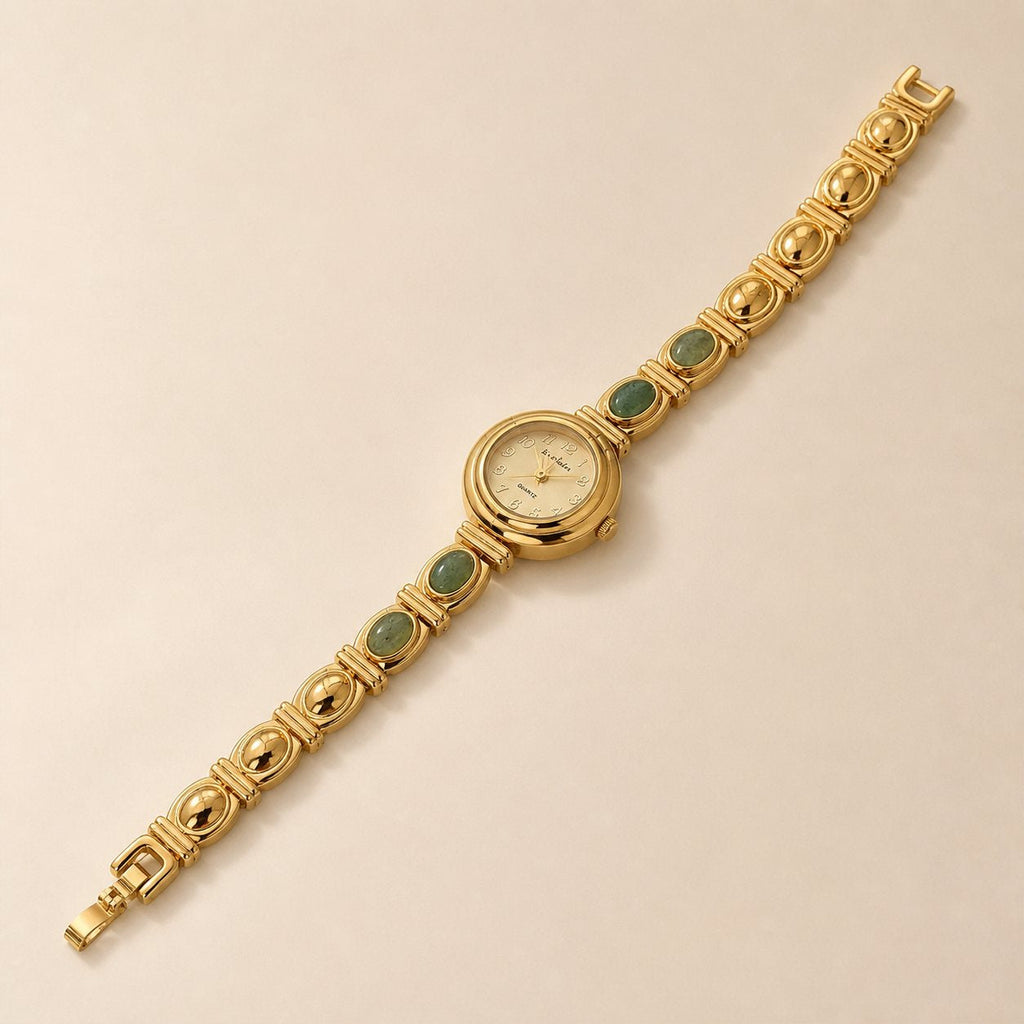 Gold-tone alloy bracelet watch with four oval green inlays arranged diagonally on a warm beige background.