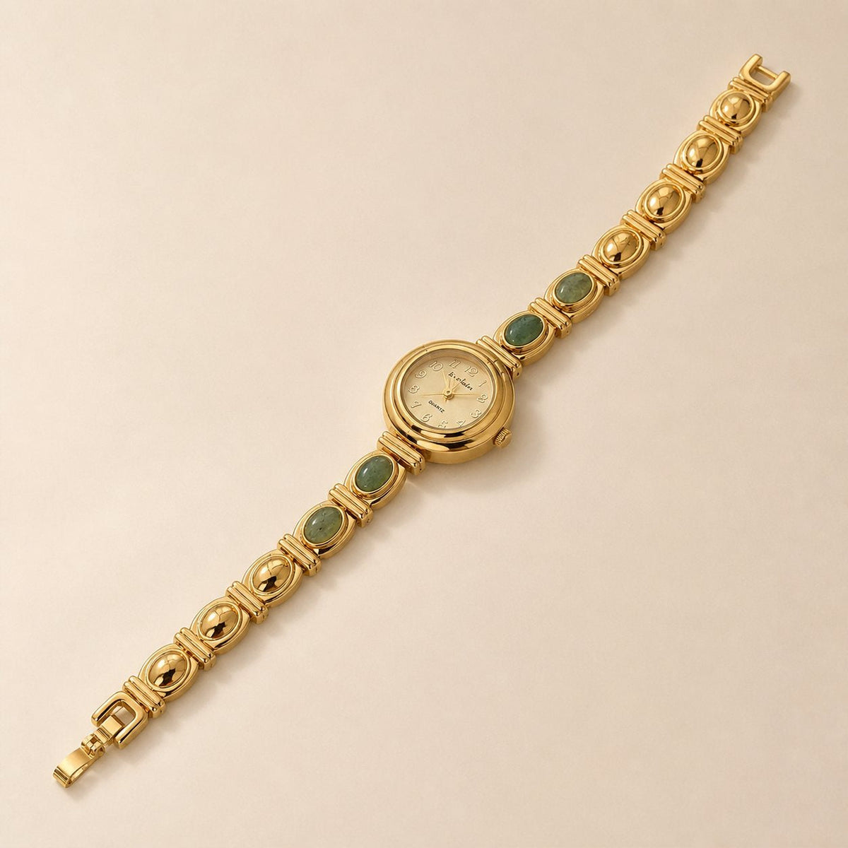 Gold-tone alloy bracelet watch with four oval green inlays arranged diagonally on a warm beige background.