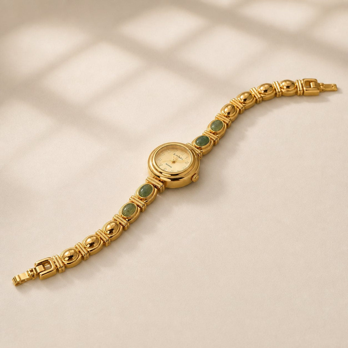Gold-tone alloy bracelet watch with four green oval inlays shown open at a three-quarter angle on beige.