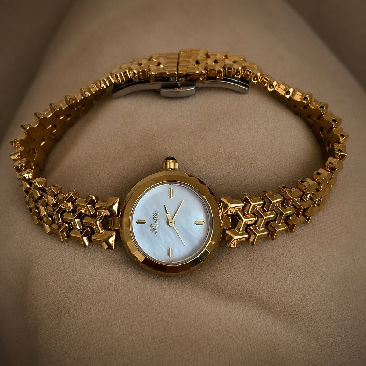 Gold-tone woven-link bracelet watch displayed in an open oval on a muted beige studio surface.