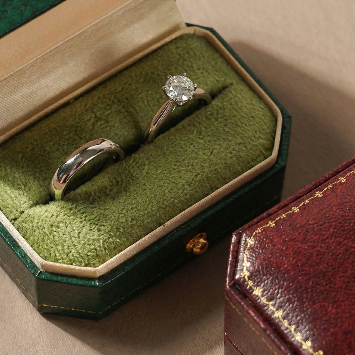 Open green ring box with a diamond solitaire ring and matching band inside, red ring box closed beside it
