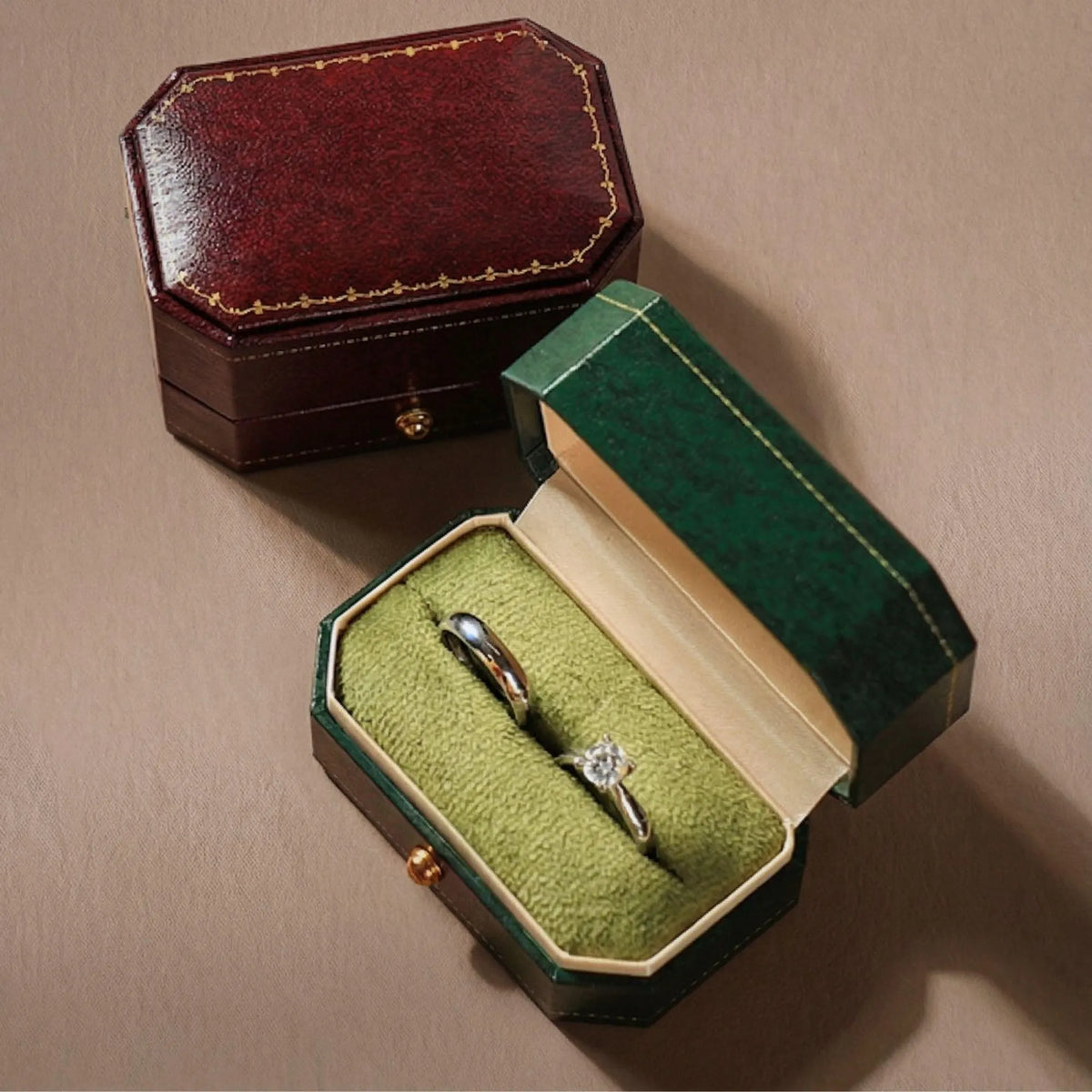 Red and green ring boxes side by side, one closed and one open showing two rings on green velvet