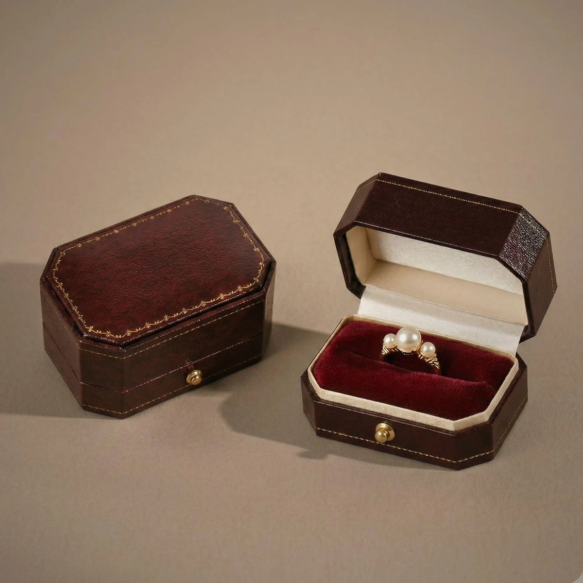 Open ring box with burgundy velvet interior and cream satin lid lining, holding a pair of pearl earrings