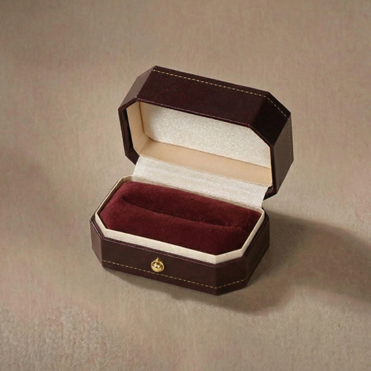 Open ring box showing the empty burgundy velvet interior and cream satin lid lining
