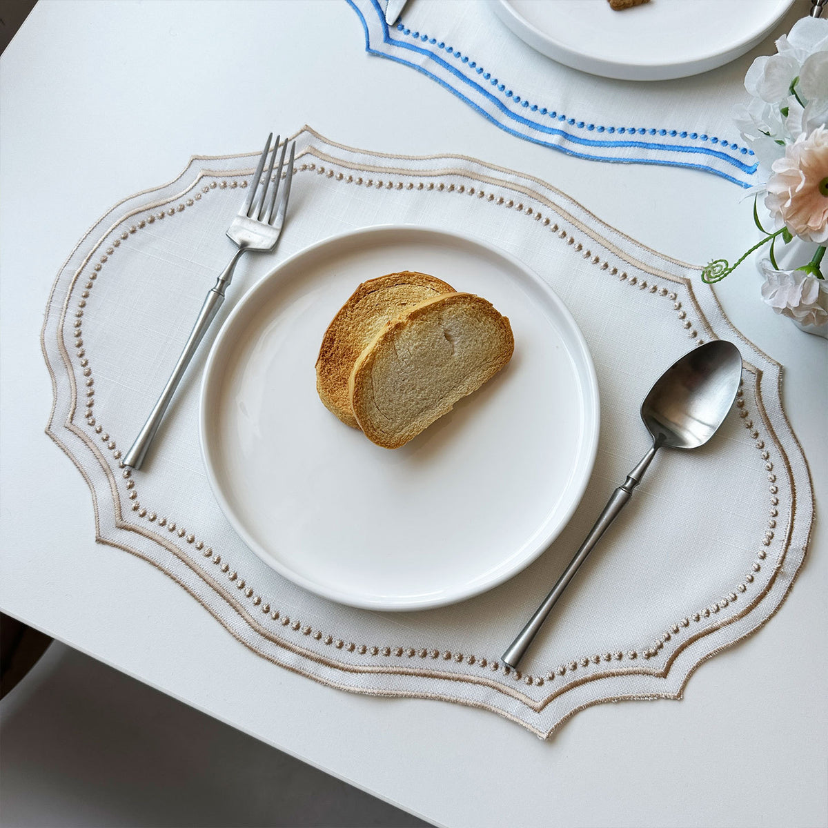 Black-trim placemat styled with gold cutlery, cherry tomatoes and tied cookies on a burlap table runner