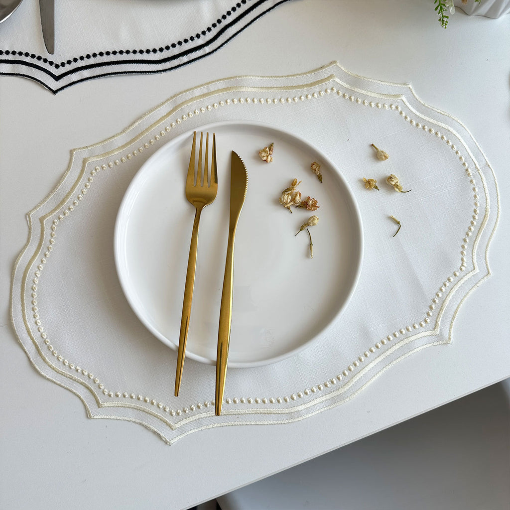 Cream-trim placemat styled with gold cutlery and dried flowers on a white plate
