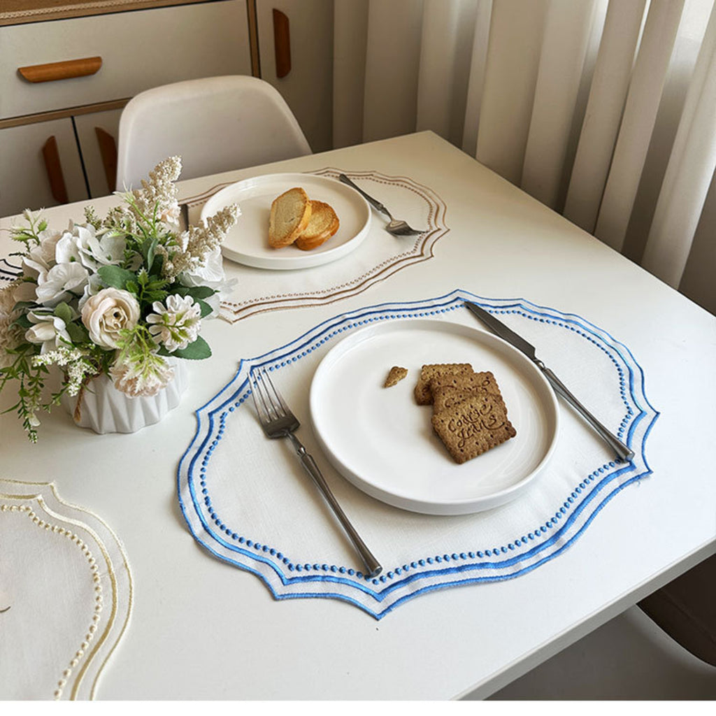 Camel-trim and sky-blue-trim placemats set with breakfast plates on a bright dining table with fresh flowers