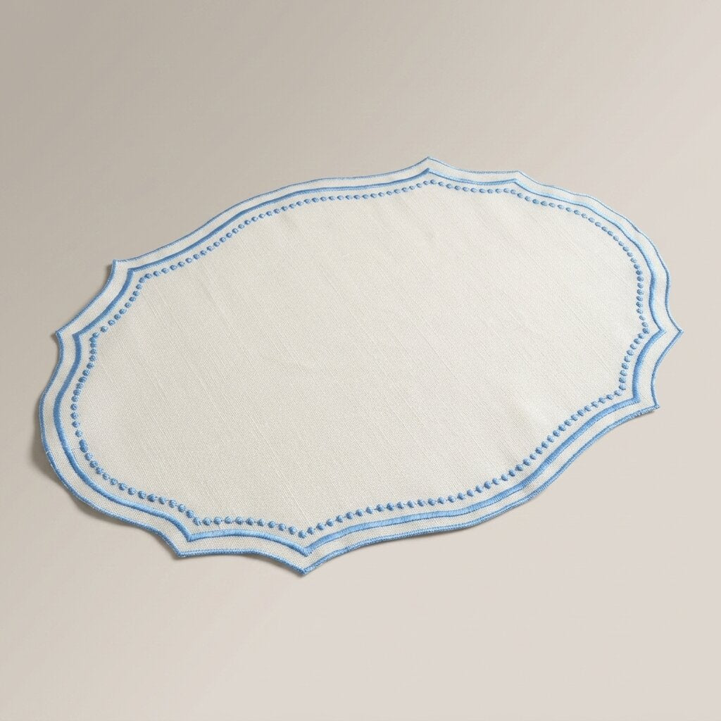Oval placemat in ivory linen-look fabric with a sky blue embroidered wavy edge, product photo