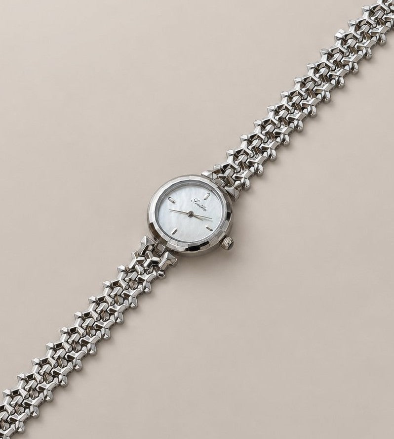 Full-length silver-tone woven-link bracelet watch laid diagonally on a muted beige studio background.