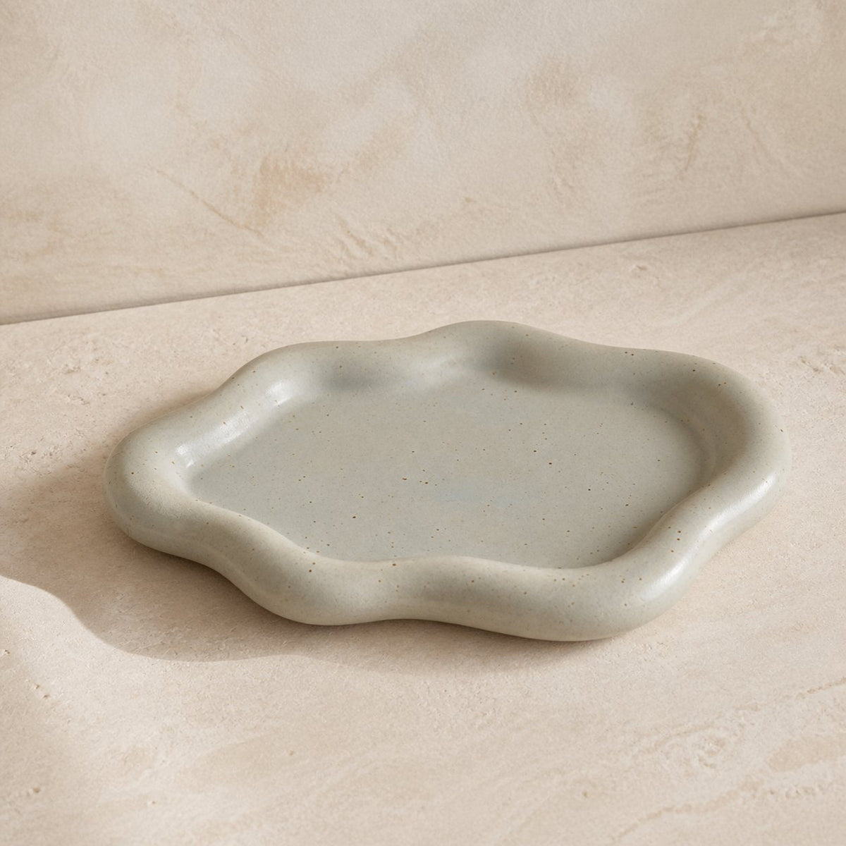 Speckled ivory cloud-shaped ceramic catchall tray viewed from a low three-quarter angle.
